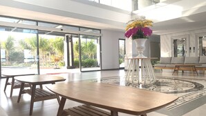 A spacious lobby with large windows, a central floral arrangement, and a seating area with a sofa and tables. - BO BIEN VANG HOTEL (Tan Thanh)