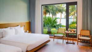 Habitación de hotel con una cama grande, una mesita con un florero y vistas a palmeras y al agua.