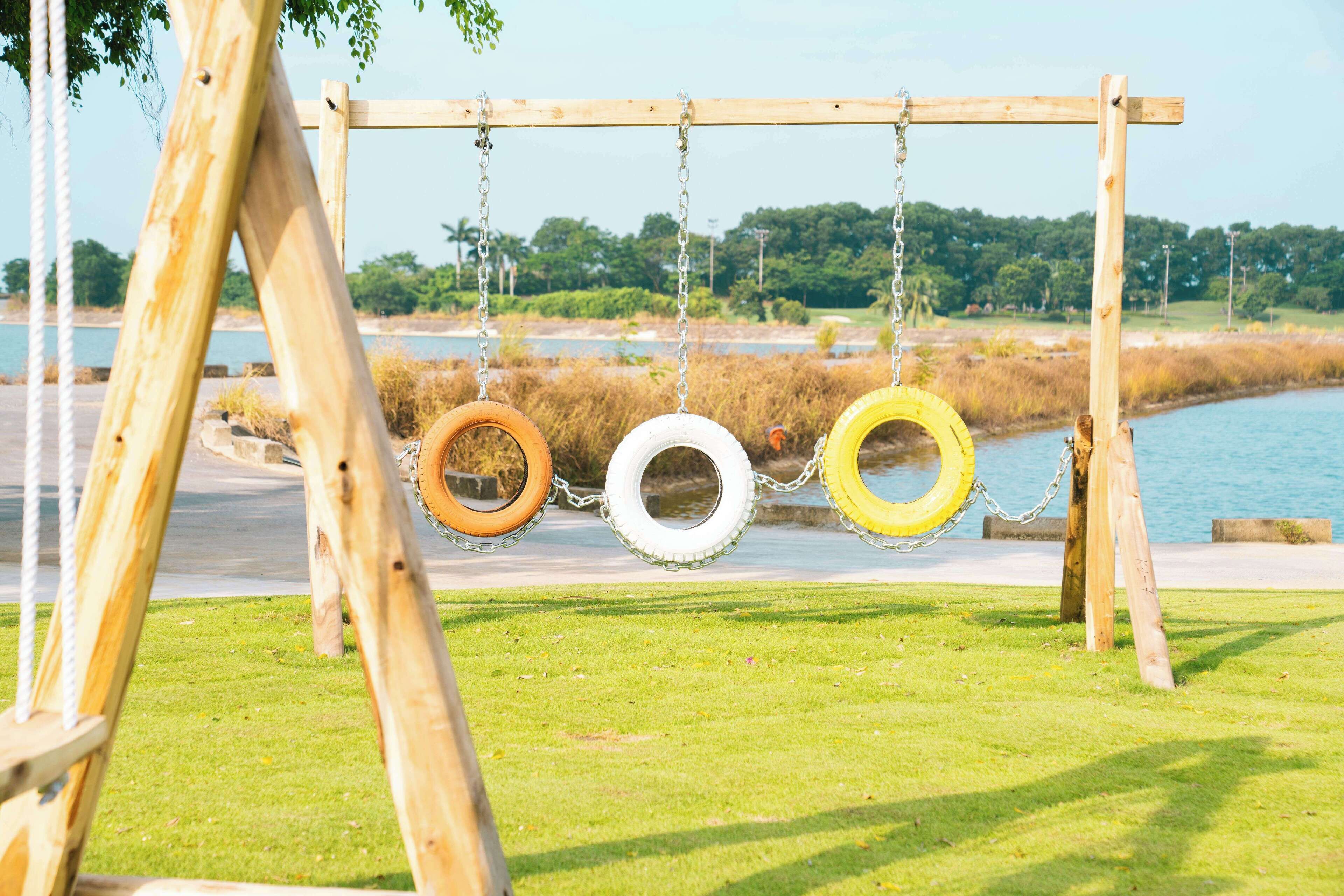 A wooden swing set with tire swings over a grassy area near a body of water.
