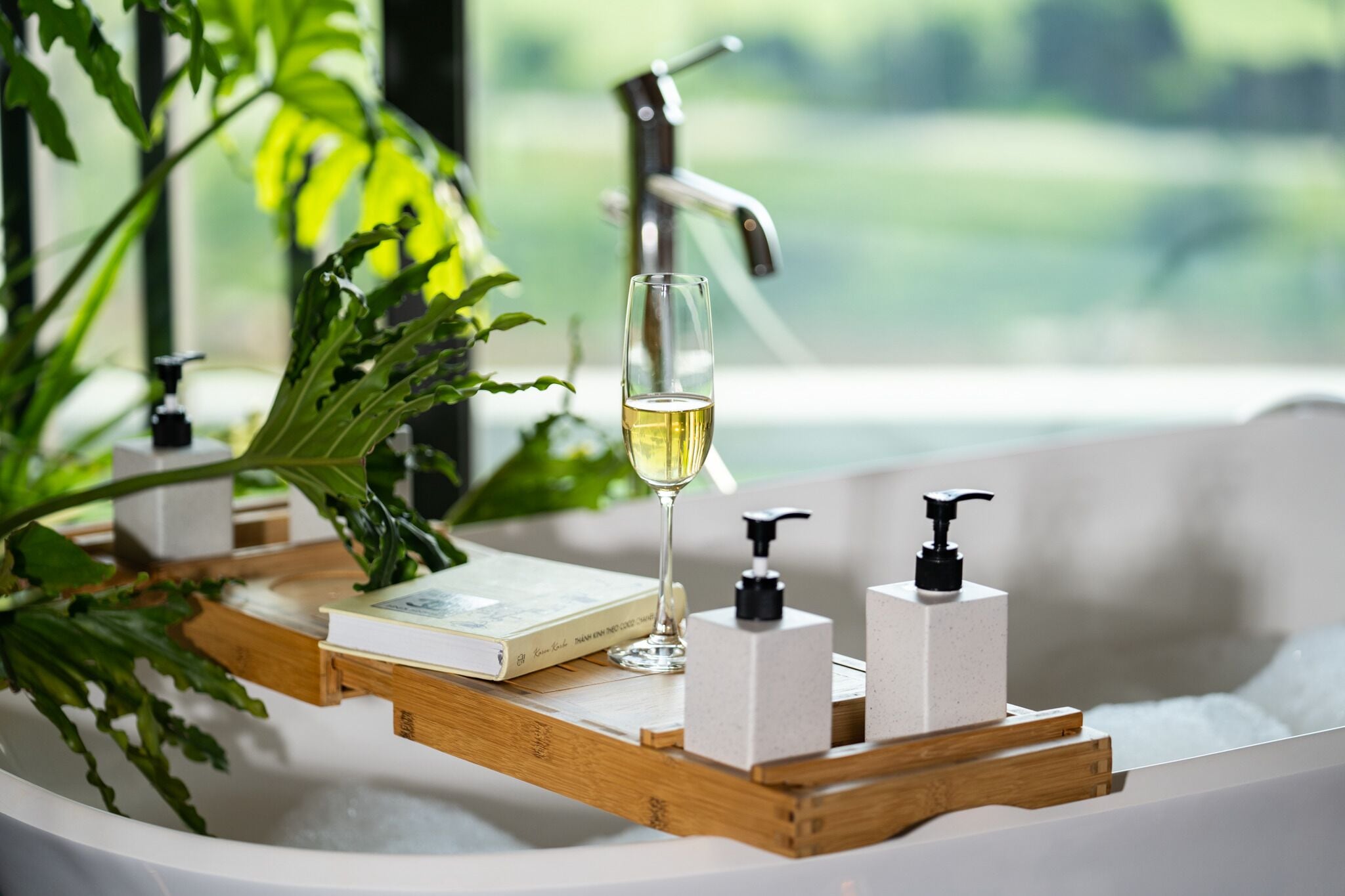 Une baignoire, un livre, un verre de vin et deux distributeurs de savon, le tout posé sur un plateau en bois.