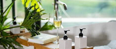 Une baignoire, un livre, un verre de vin et deux distributeurs de savon, le tout posé sur un plateau en bois.