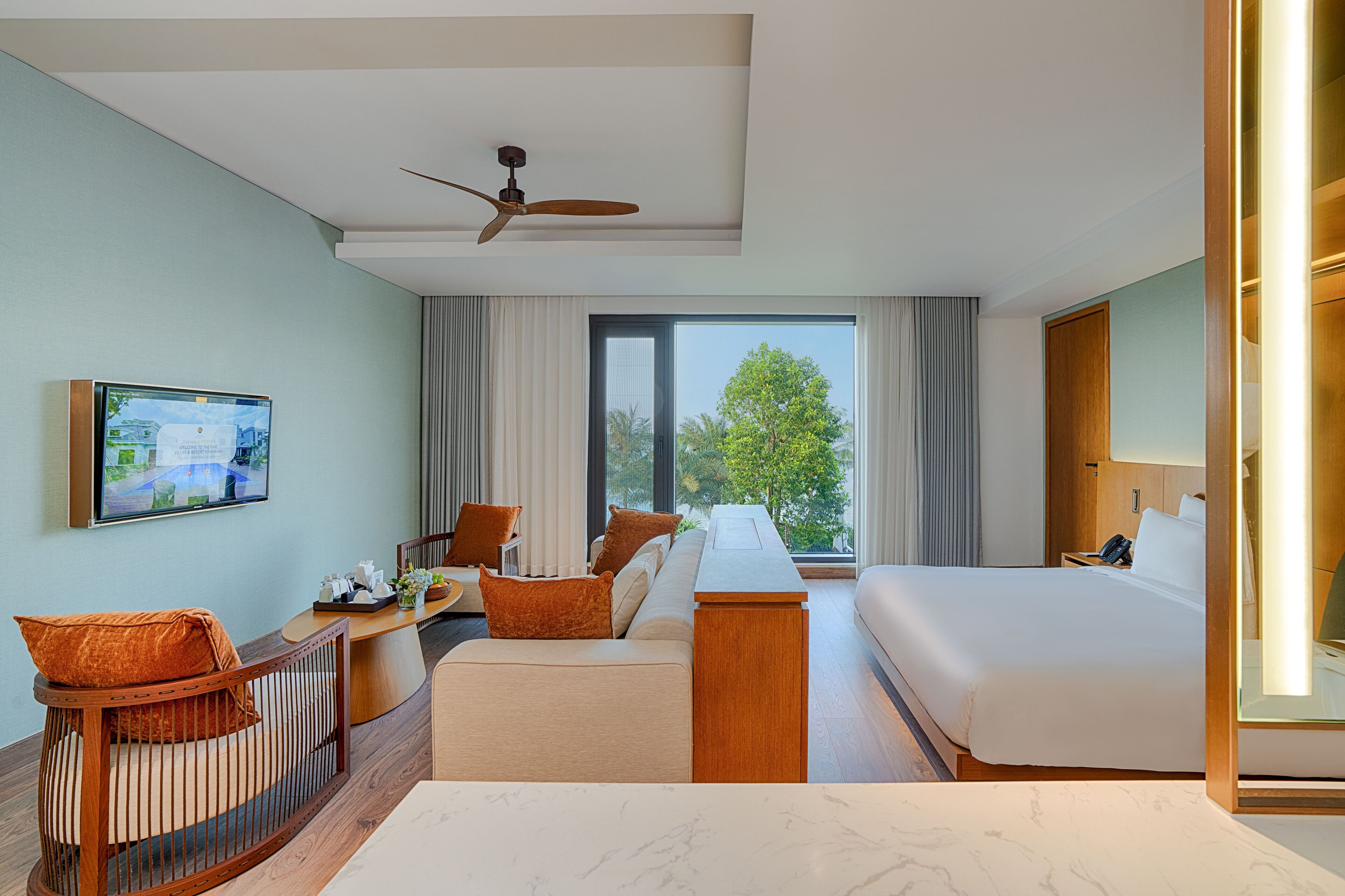Habitación de hotel con cama, escritorio, silla, televisor y vistas al exterior.