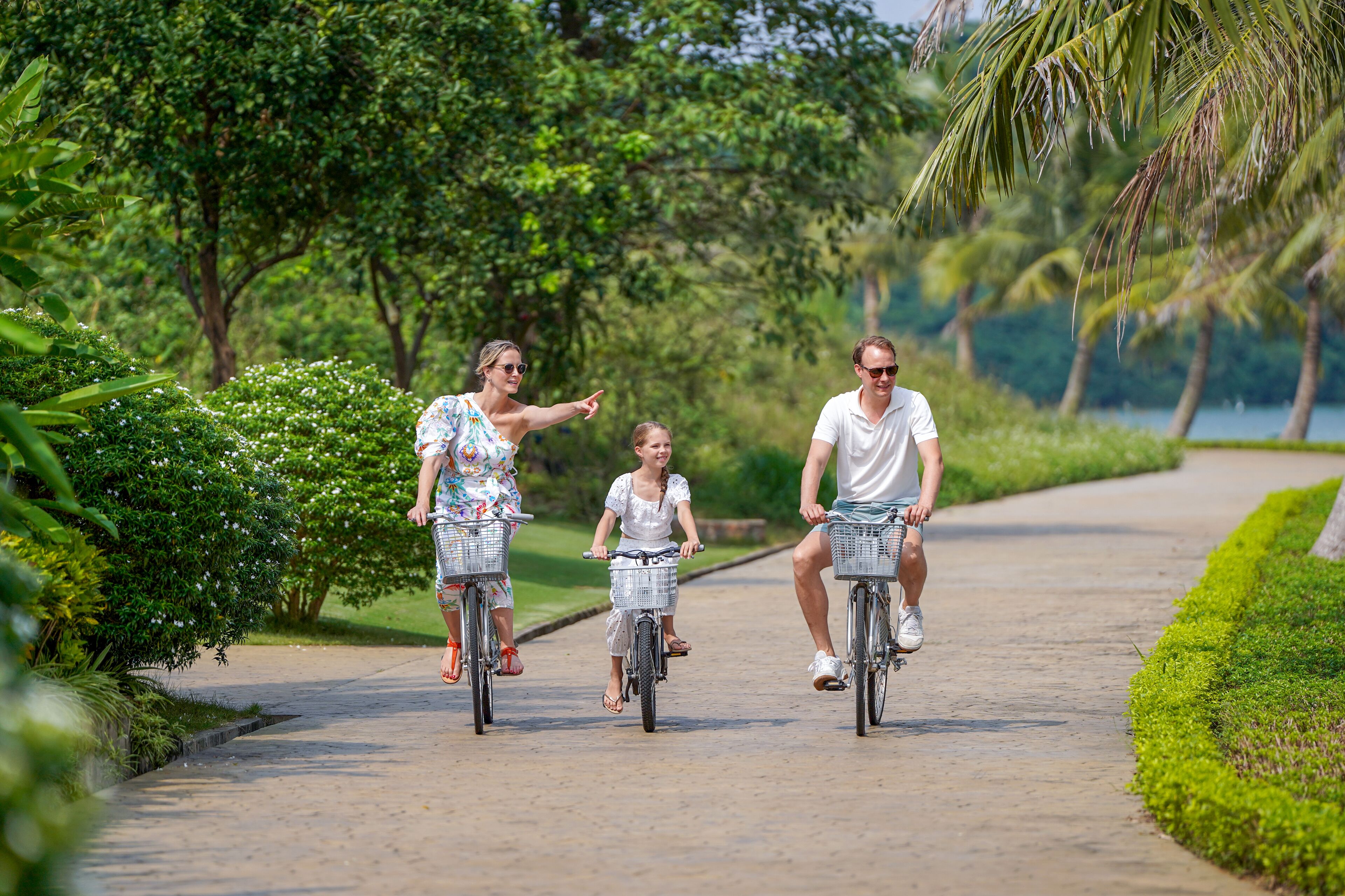 Three people riding bicycles on a paved path surrounded by greenery.