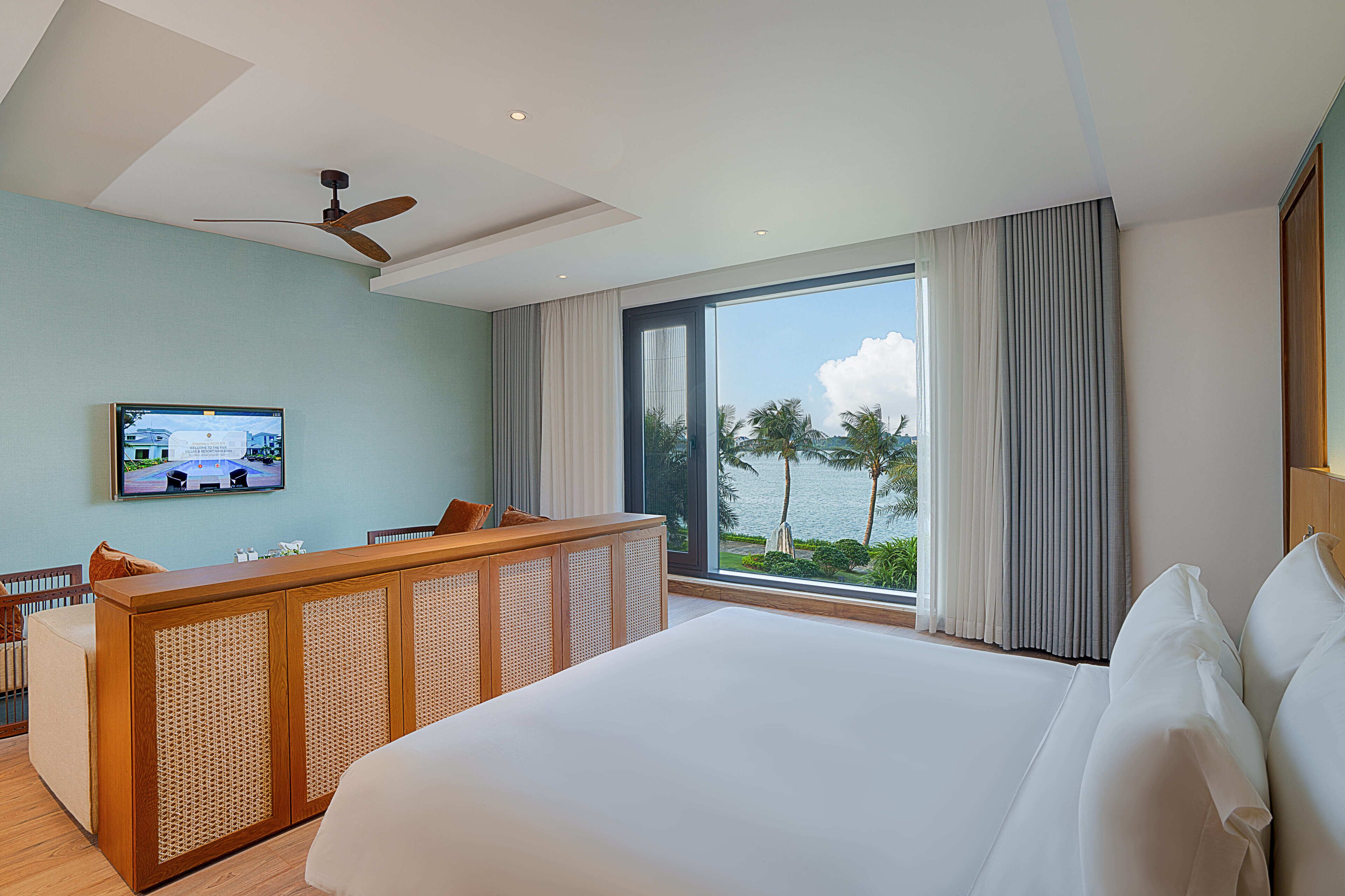 A hotel room with a large bed, a wooden desk, a television, and a view of the sea.