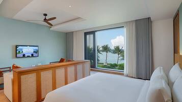 A hotel room with a large bed, a wooden desk, a television, and a view of the sea.