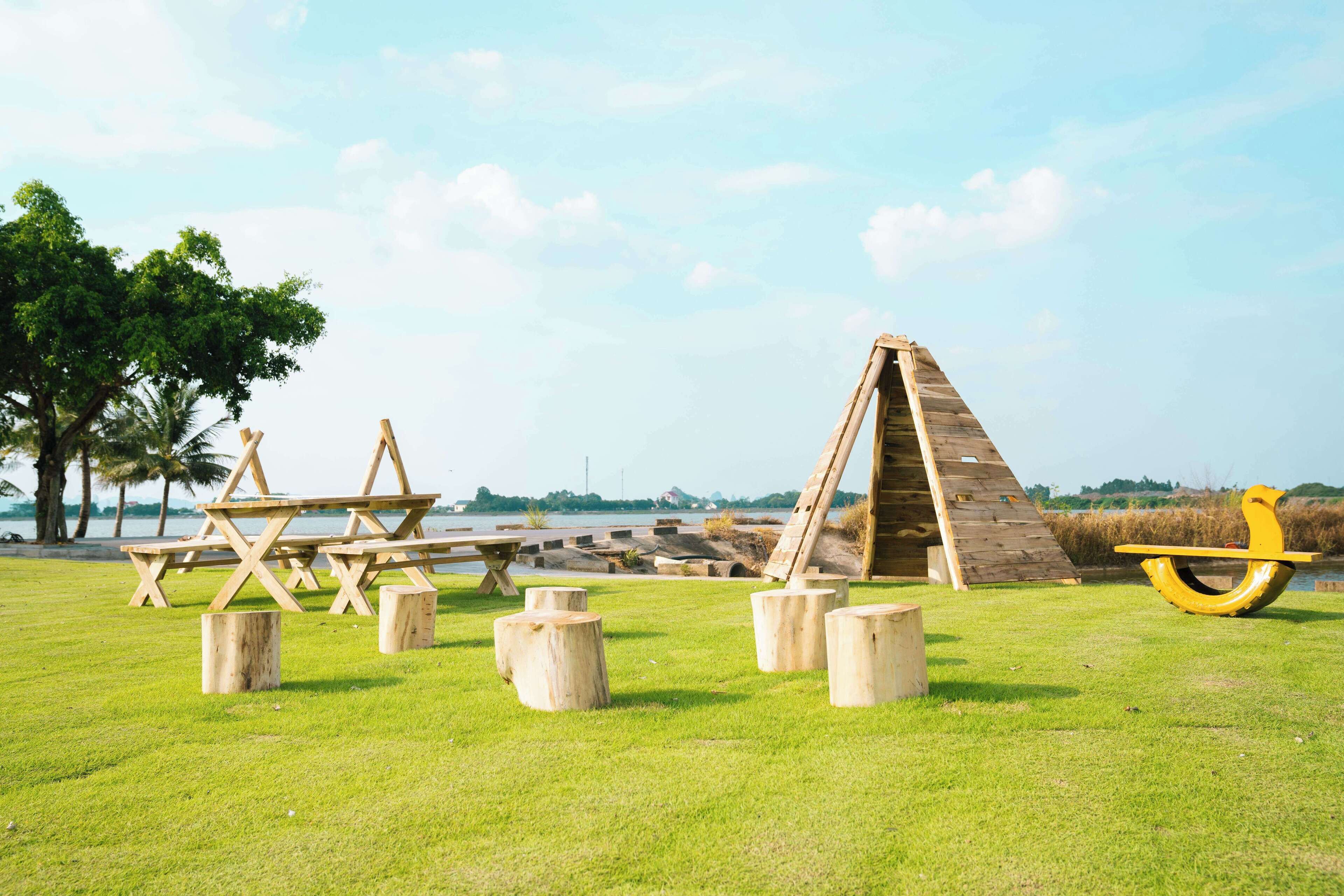 A picnic area with wooden tables and benches, a wooden climbing structure, and a yellow sculpture.