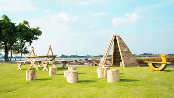 A picnic area with wooden tables and benches, a wooden climbing structure, and a yellow sculpture.