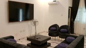Un salon moderne avec un téléviseur à écran plat, deux fauteuils, un canapé et une table basse.