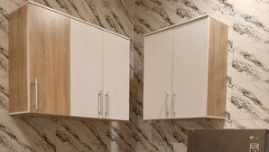 Une cuisine avec des murs décorés d’un motif imitant le marbre, deux armoires en bois, un four à micro-ondes noir et un réfrigérateur en acier inoxydable.