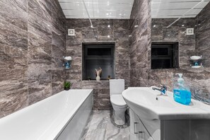 A modern bathroom with a bathtub, toilet, and sink, featuring marble walls and a ceiling with recessed lighting. - 2 Bed Flat - Sleeps 8 - Pets - Parking - Wifi (Blackpool)