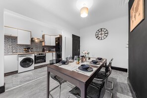 A modern kitchen with a dining area, featuring a large table set for four, a built-in oven, and a washing machine. - 2 Bed Flat - Sleeps 8 - Pets - Parking - Wifi (Blackpool)
