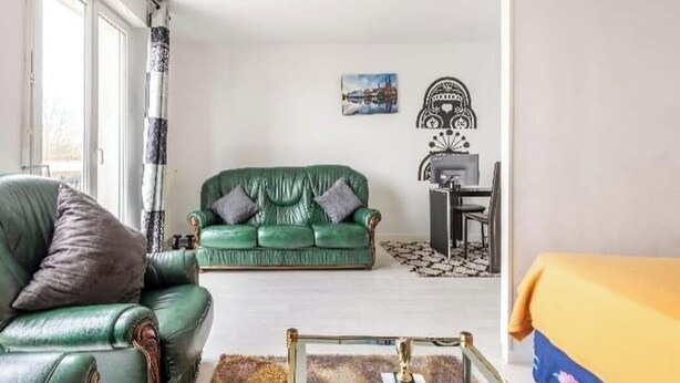 Ein Wohnzimmer mit einem grünen Sofa, einem grünen Sessel, einem kleinen Tisch und einem dekorativen Wandbild.