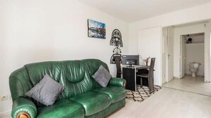 Ein grünes Ledersofa mit zwei Kissen, ein kleiner Tisch mit einem Fernseher und eine weiße Tür zu einem Badezimmer.