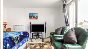 Ein Wohnzimmer mit einer Couch, einem Couchtisch, einem Flachbildfernseher, einem Bett mit gemustertem Überwurf und einem Bild an der Wand.
