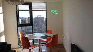 A dining area with a round table, four orange chairs, and a view of a cityscape through large windows. - Apartment - Sleeps 4 - Pet friendly - WiFi (Sheffield)