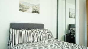 A bedroom with a bed, a gray headboard, striped bedding, a painting of a landscape, and a sliding door. - Apartment - Sleeps 4 - Pet friendly - WiFi (Sheffield)