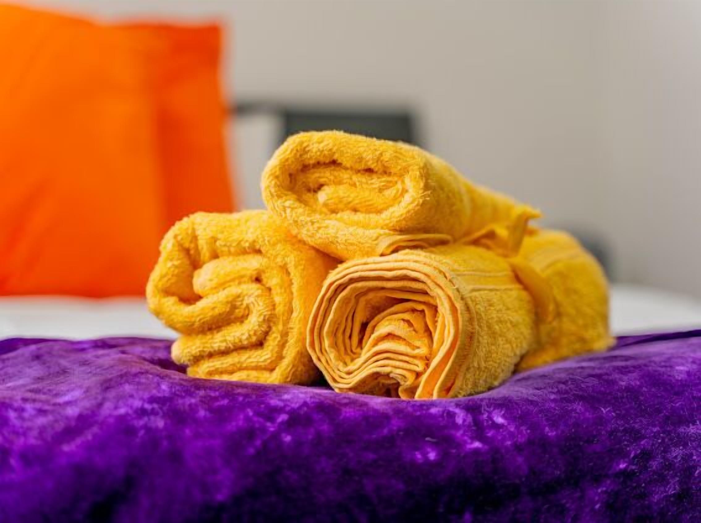 Un lit avec des serviettes jaunes roulées et une couverture violette.