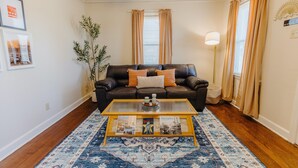 Ein Wohnzimmer mit einem dunkelbraunen Ledersofa, einem Glastisch und einem gemusterten Teppich.