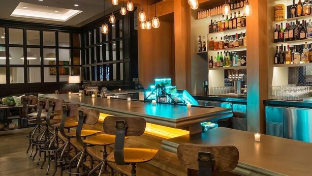 A bar area with a long counter, multiple stools, and a well-stocked liquor shelf.