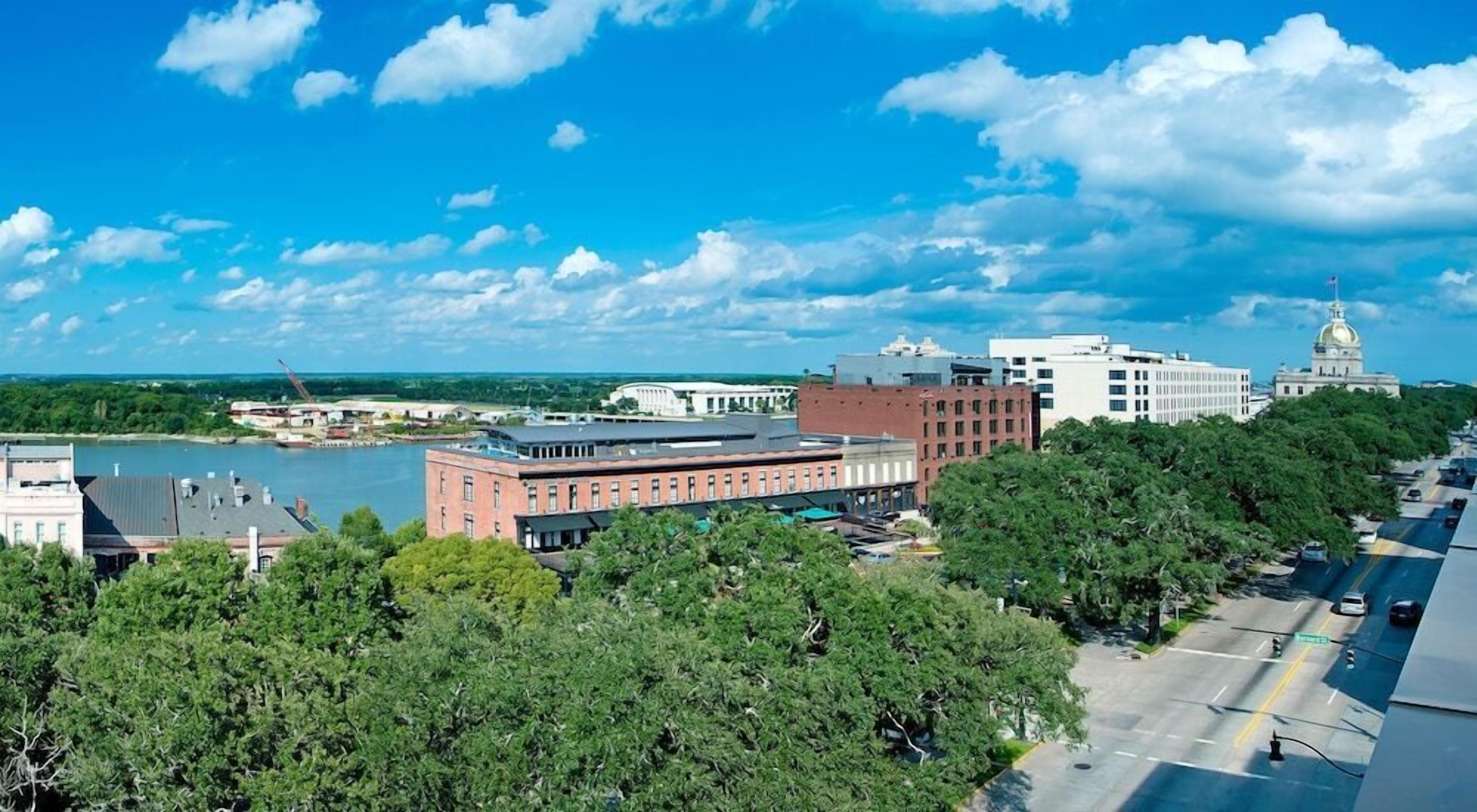 A cityscape with a prominent building with a dome, a river, and lush green trees.