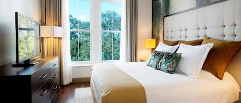 A bedroom with a large bed, a television on a dresser, and a window with curtains.