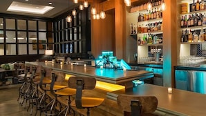 A bar area with a long counter, multiple stools, and a well-stocked liquor shelf. - 1-Bedroom Suite at a 4⭐️ Hotel (Savannah)