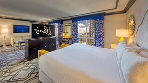 Habitación de hotel con una cama grande, televisión, escritorio con silla, espejo y vistas a la ciudad desde la ventana.