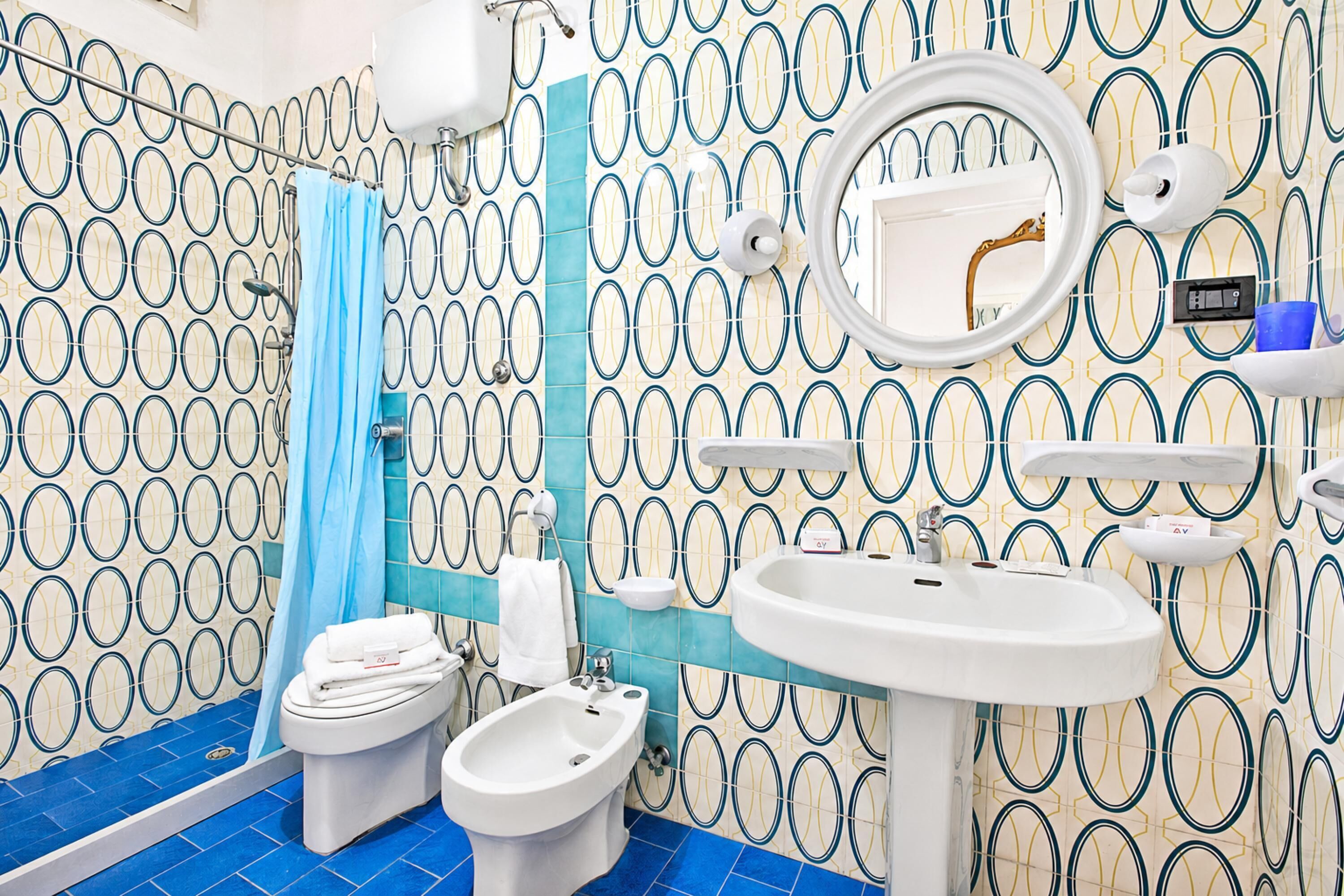 A bathroom with a toilet, bidet, sink, mirror, and patterned walls.