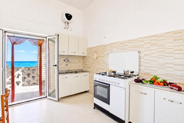 Une cuisine avec vue sur la mer, équipée d’une cuisinière, d’un four et comprenant un coin repas avec une chaise.