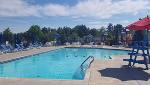 A swimming pool with blue lounge chairs, a lifeguard stand, and a red umbrella.