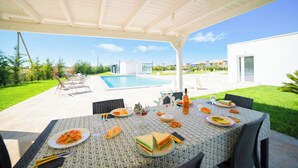 An outdoor patio with a table set for a meal, a pool, and a modern house in the background. - Villa Cristal Pool and Padel, Galatina, Italy (Galatina)
