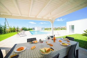 An outdoor dining area with a pool, covered patio, and modern architecture.