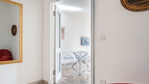 A hallway with a mirror, a red chair, and a table with transparent chairs. - Relais Vittoriale (Gardone Riviera)