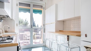 A kitchen with a gas stove, white cabinets, and a sliding glass door leading to an outdoor patio. - Relais Vittoriale (Gardone Riviera)