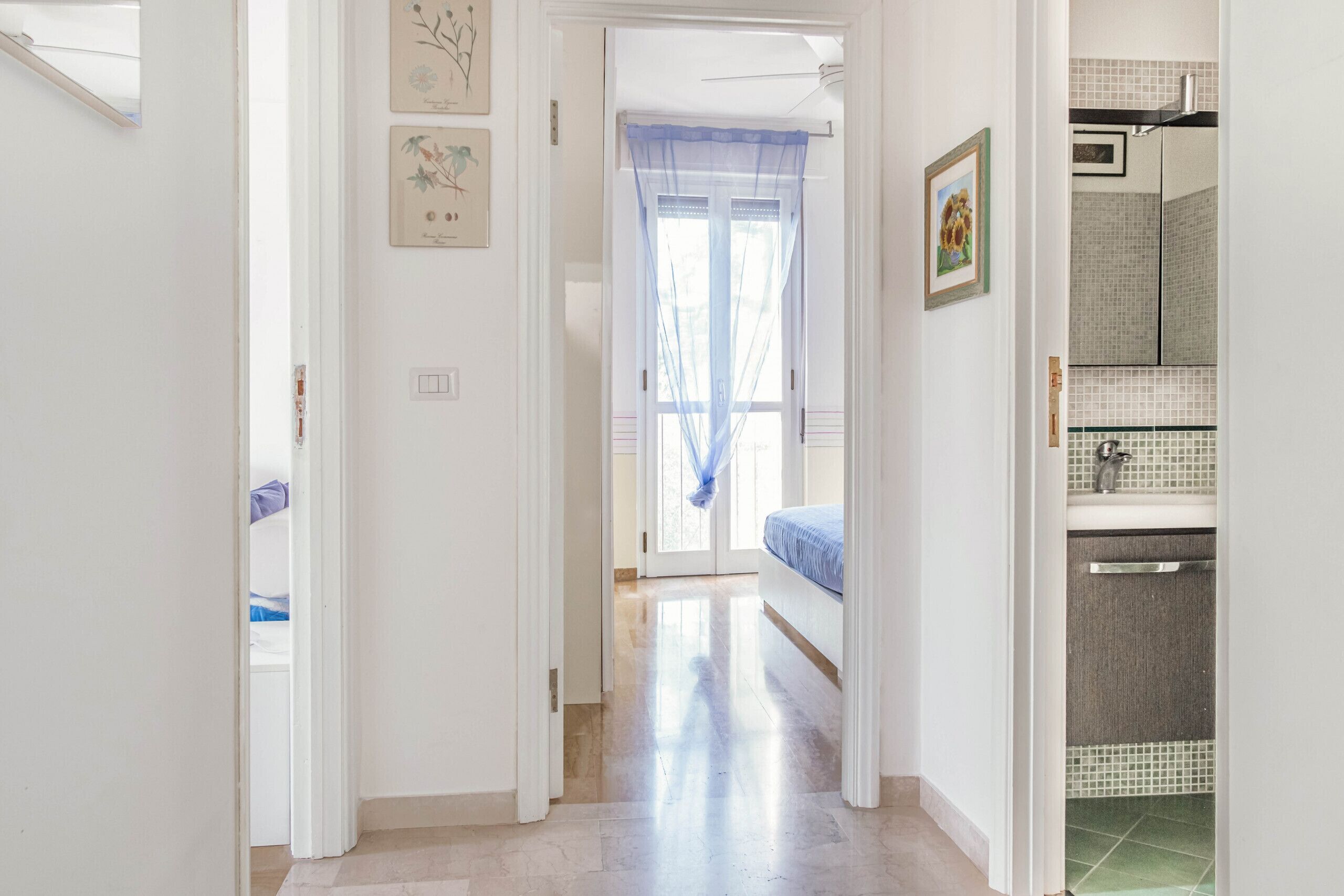 A hallway leading to a bedroom with a bed, a bathroom with a shower, and a door leading to another room.