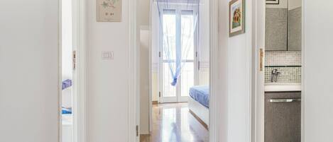 A hallway leading to a bedroom with a bed, a bathroom with a shower, and a door leading to another room.