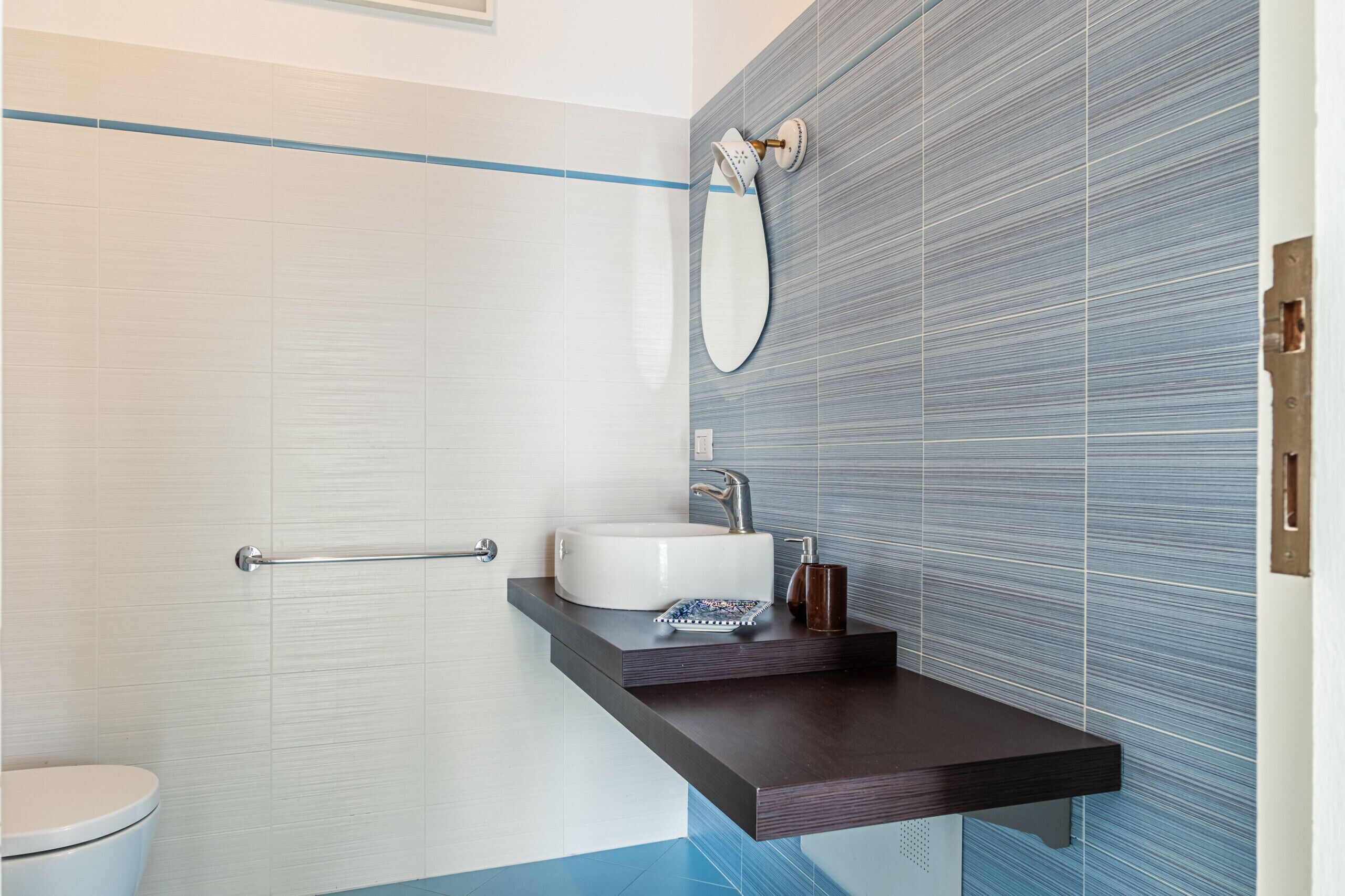 Une salle de bain avec des toilettes blanches, un lavabo doté d’un plan-vasque foncé et un mur recouvert de carreaux bleus.