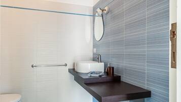 Une salle de bain avec des toilettes blanches, un lavabo doté d’un plan-vasque foncé et un mur recouvert de carreaux bleus.