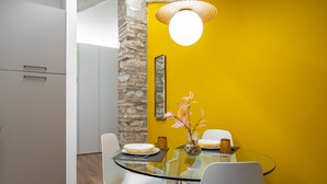 Un área de comedor con una mesa de vidrio, sillas blancas, una pared amarilla y una pared de acento de piedra.