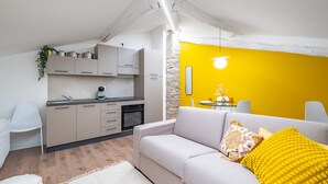 Una cocina moderna con armarios de colores claros, un comedor con pared de acento amarilla y una zona de estar acogedora con sofá y cojines.
