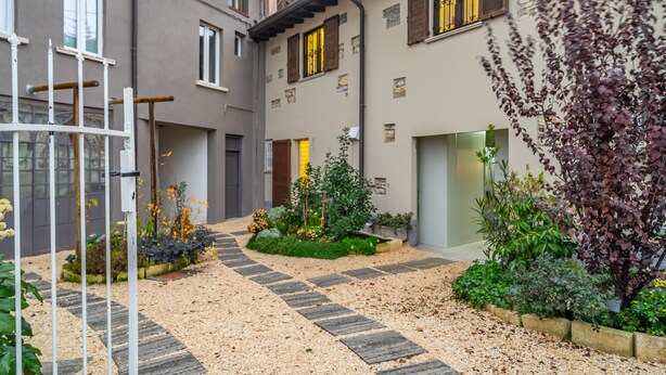 Un patio con sendero de grava, plantas en macetas y una reja metálica.