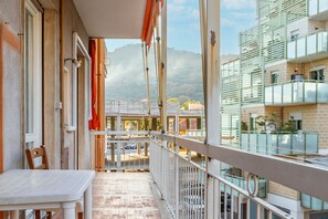 A balcony with a table and chairs, overlooking a street and buildings with a mountainous backdrop. - Il Foreste 'Foesto' (Imperia)