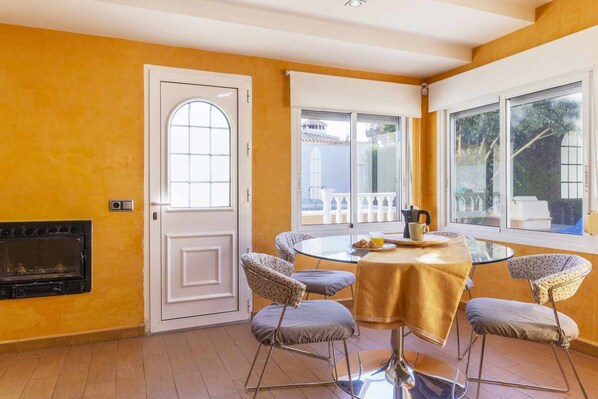 A room with a round table, four chairs, a fireplace, and large windows with a view. - Villa PINK VILLACOSTA (Torrevieja)