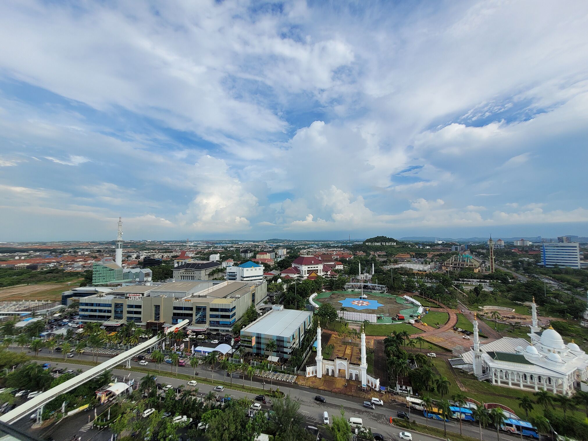 A cityscape with a prominent mosque, a large building with a blue roof, and a road with vehicles.