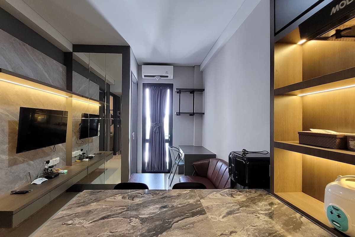 Ein modernes Hotelzimmer mit Marmorboden, einem an der Wand montierten Flachbildfernseher, einem Schreibtisch mit Telefon und einer kleinen Küchenzeile.