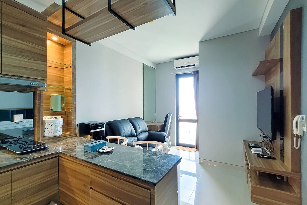 Eine moderne Küche mit Holzausbau, einer Marmorarbeitsplatte und einem eingebauten Backofen. Es gibt eine Sitzecke mit einer schwarzen Ledersofa und einem kleinen Tisch.