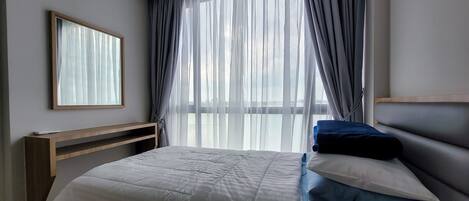 Un dormitorio con cama, mesita de noche, espejo y ventana con cortinas traslúcidas.