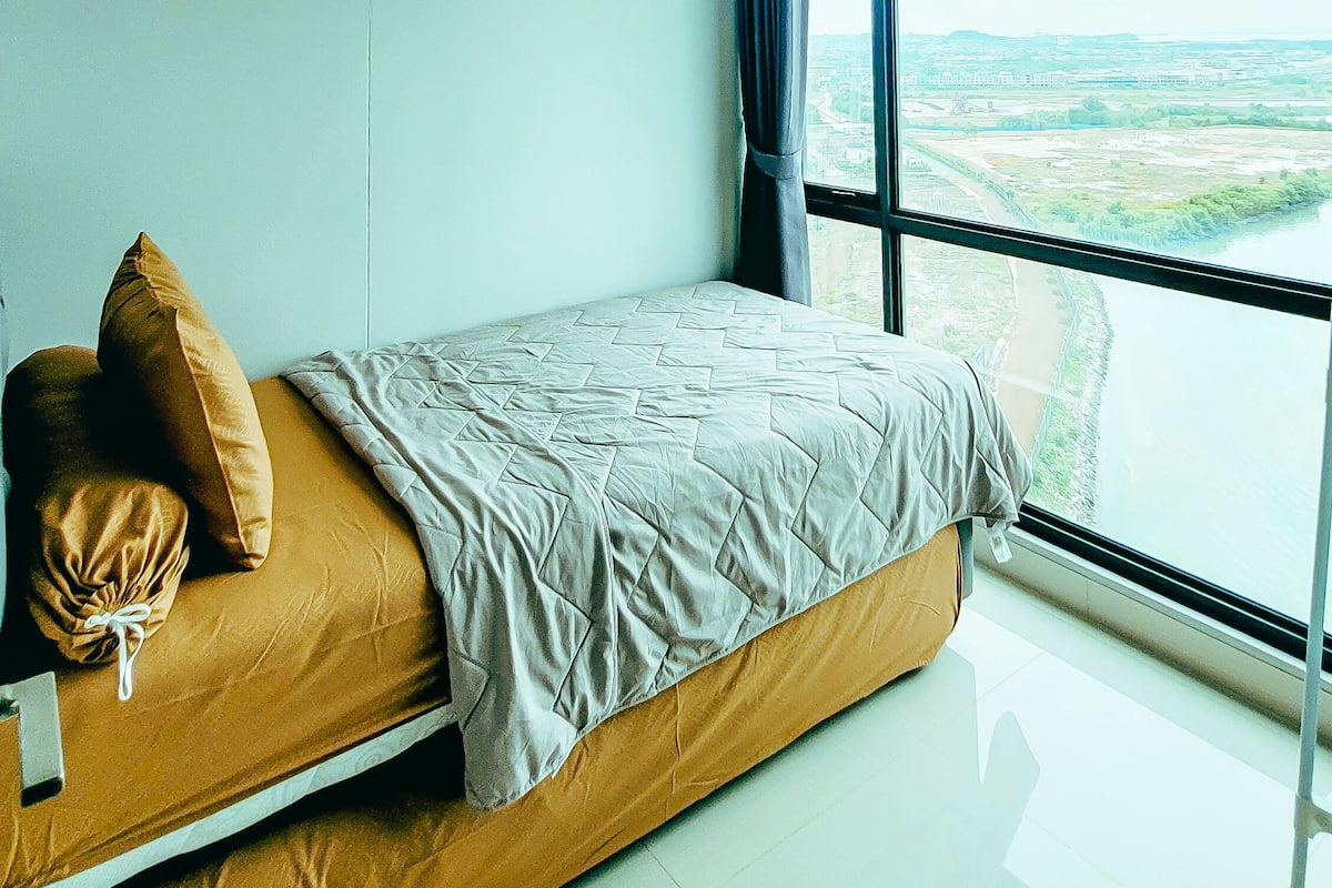 Ein modernes Schlafzimmer mit Bett, Blick auf eine Stadtlandschaft durch große Fenster und einer Decke mit zwei Rauchmeldern.
