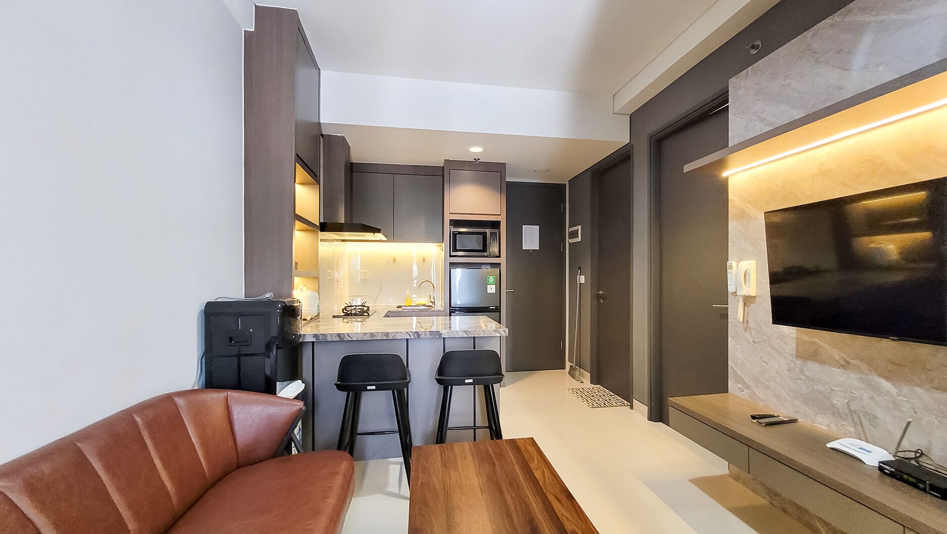 A modern kitchen with a central island, a dining area with a sofa and chairs, and a living area with a TV.