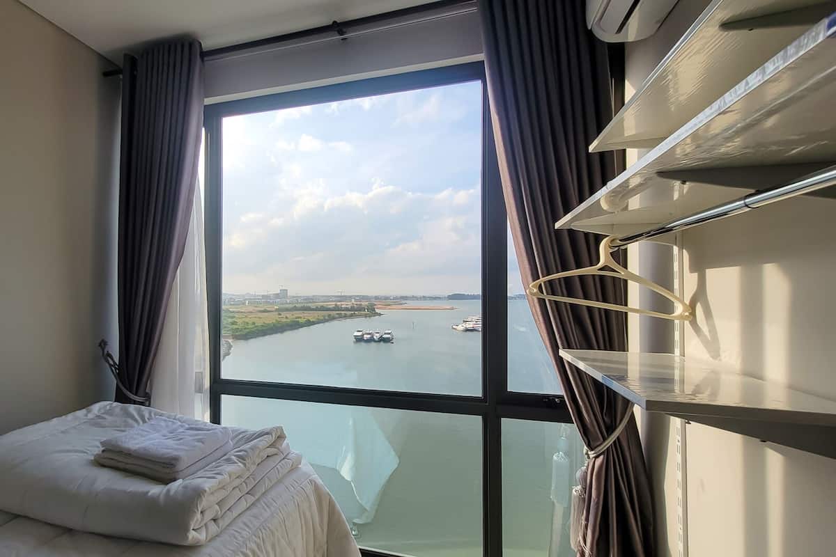 Ein Hotelzimmer mit großem Fenster, einem Bett mit weißer Bettwäsche, einem Nachttisch und einer Hängelampe.